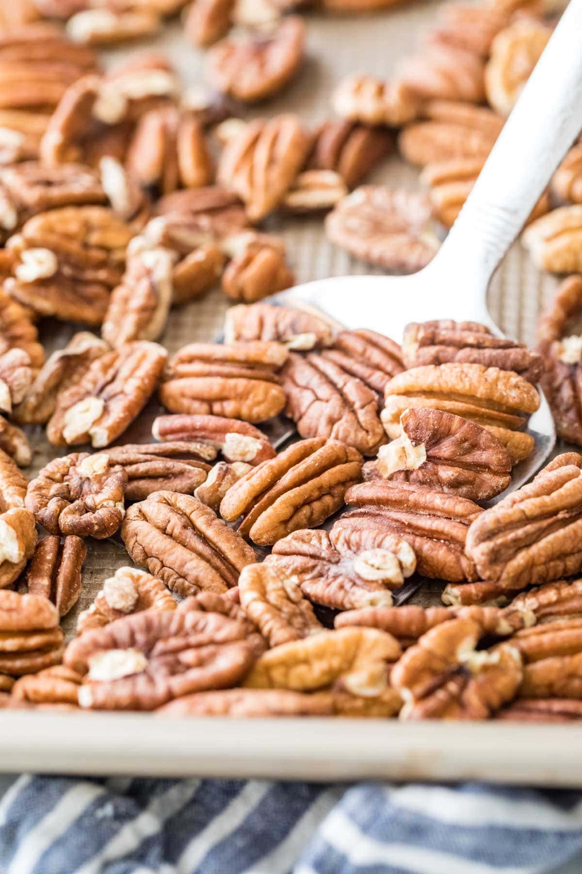 photo showing how to toast pecans in the oven, with a metal spatula about to flip whole pecans on a baking sheet