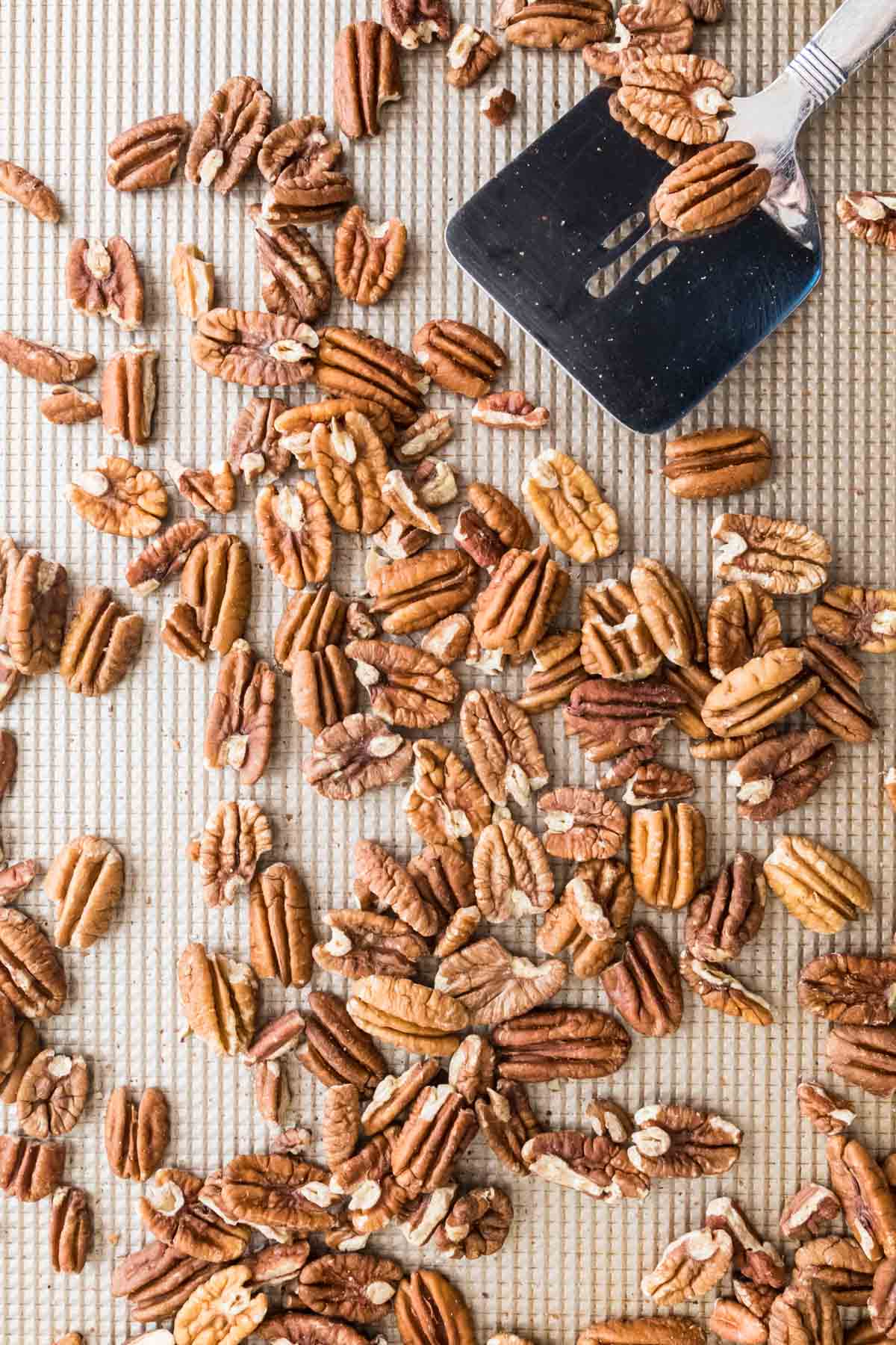 whole pecans scattered on a baking sheet after being tossed by a spatula