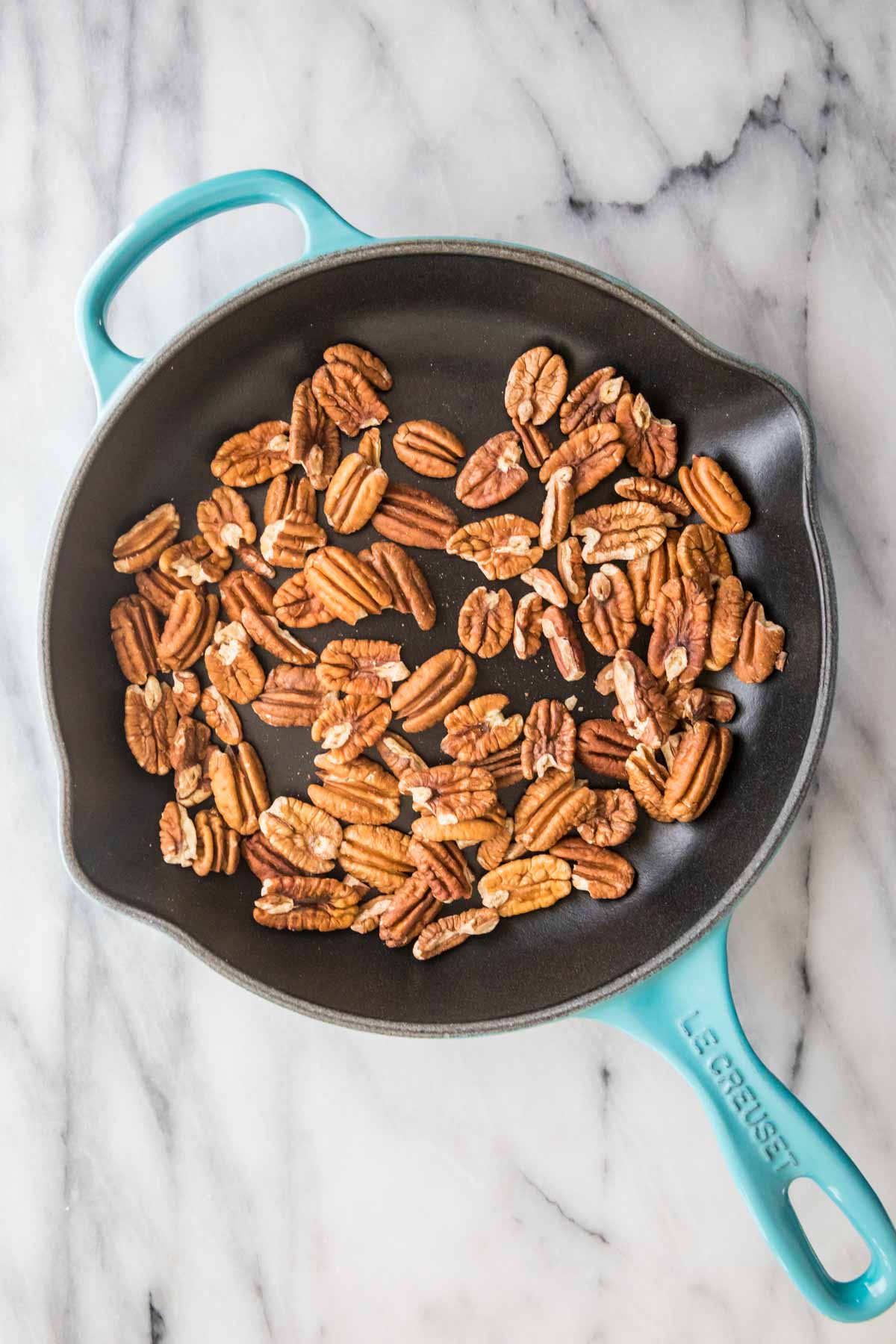 whole pecans in a bright aqua cast iron skillet