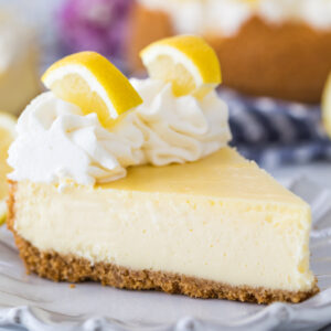 slice of lemon cheesecake topped with whipped cream and sliced lemon wedges