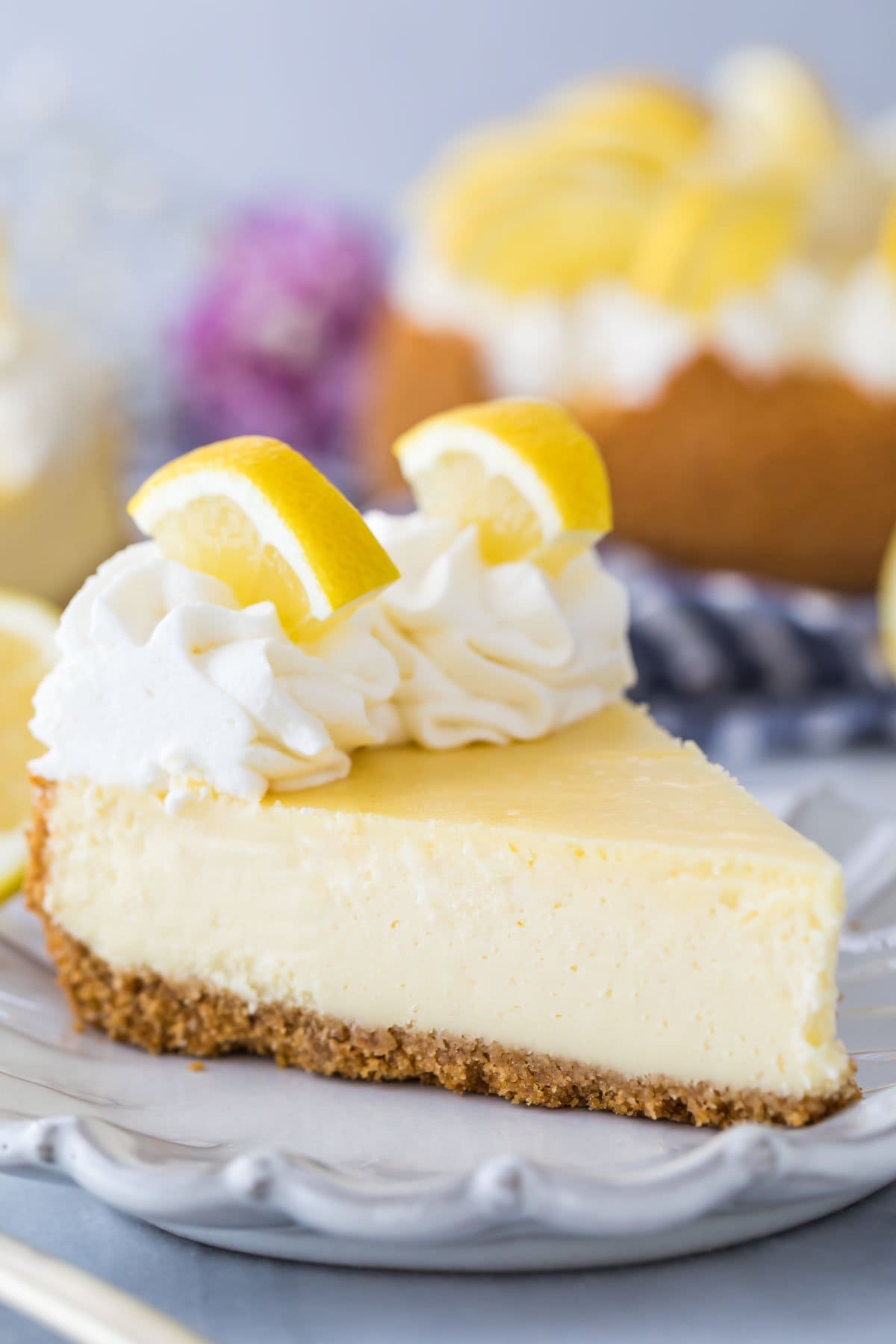 slice of lemon cheesecake topped with whipped cream and sliced lemon wedges