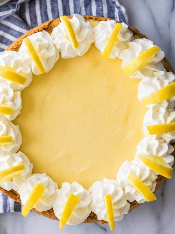 overhead view of a whole lemon cheesecake decorated with whipped cream and lemon slices