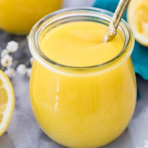 close-up view of a glass jar filled with bright yellow curd with a spoon dipped into it