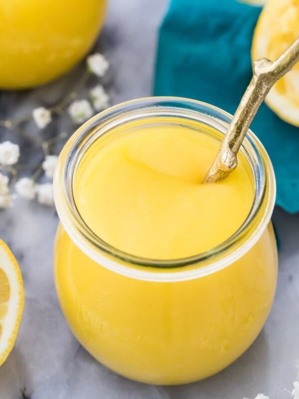 glass jar full of homemade lemon curd on a gray marble surface surrounded by lemon halves and small white baby's breath flowers
