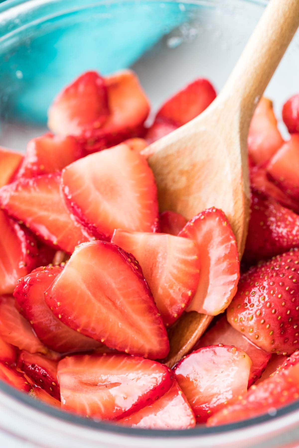 wooden spoon stirring sliced macerated strawberries in a clear bowl