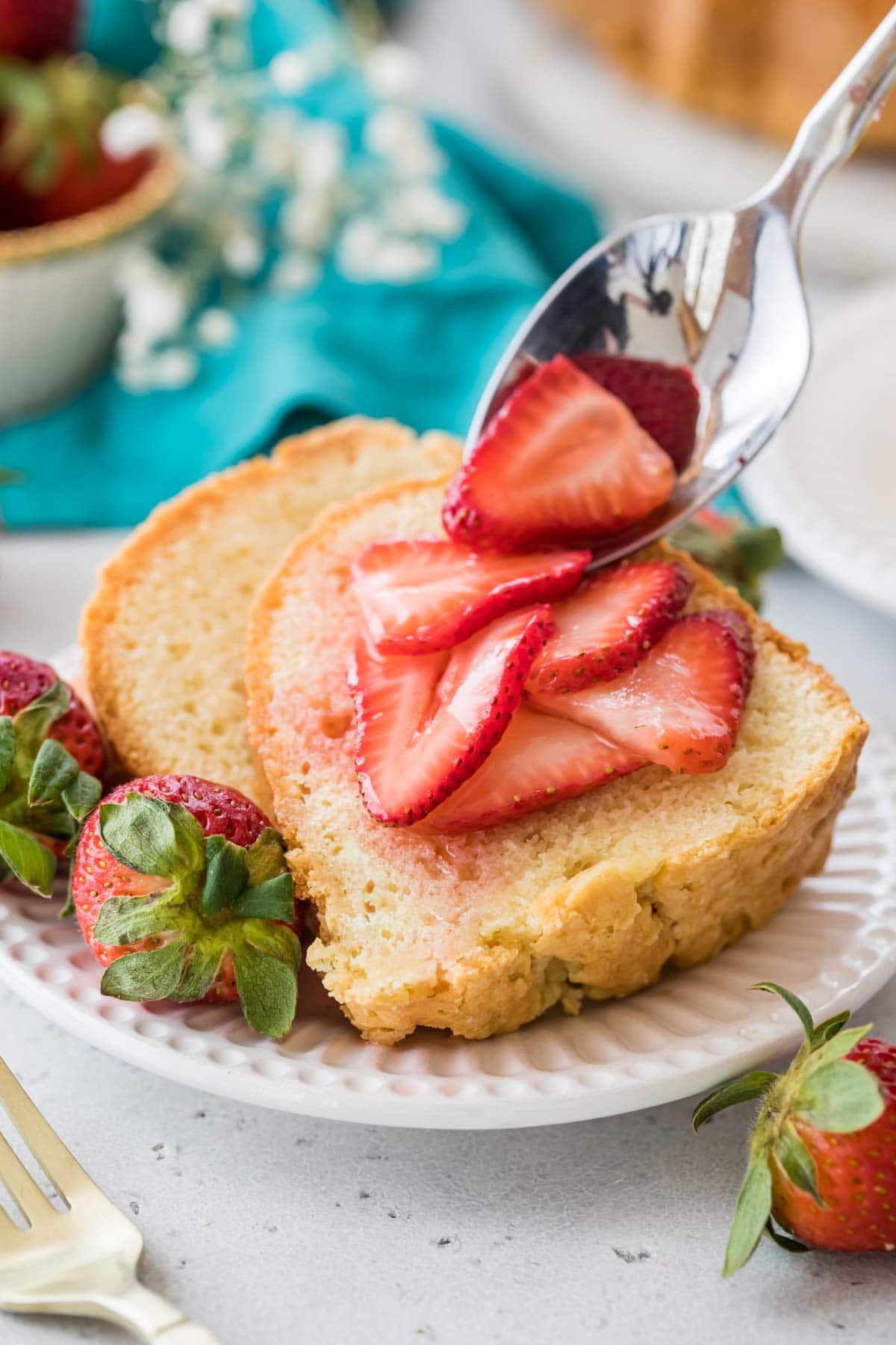 macerated strawberries being spooned onto two slices of cake on a white plate