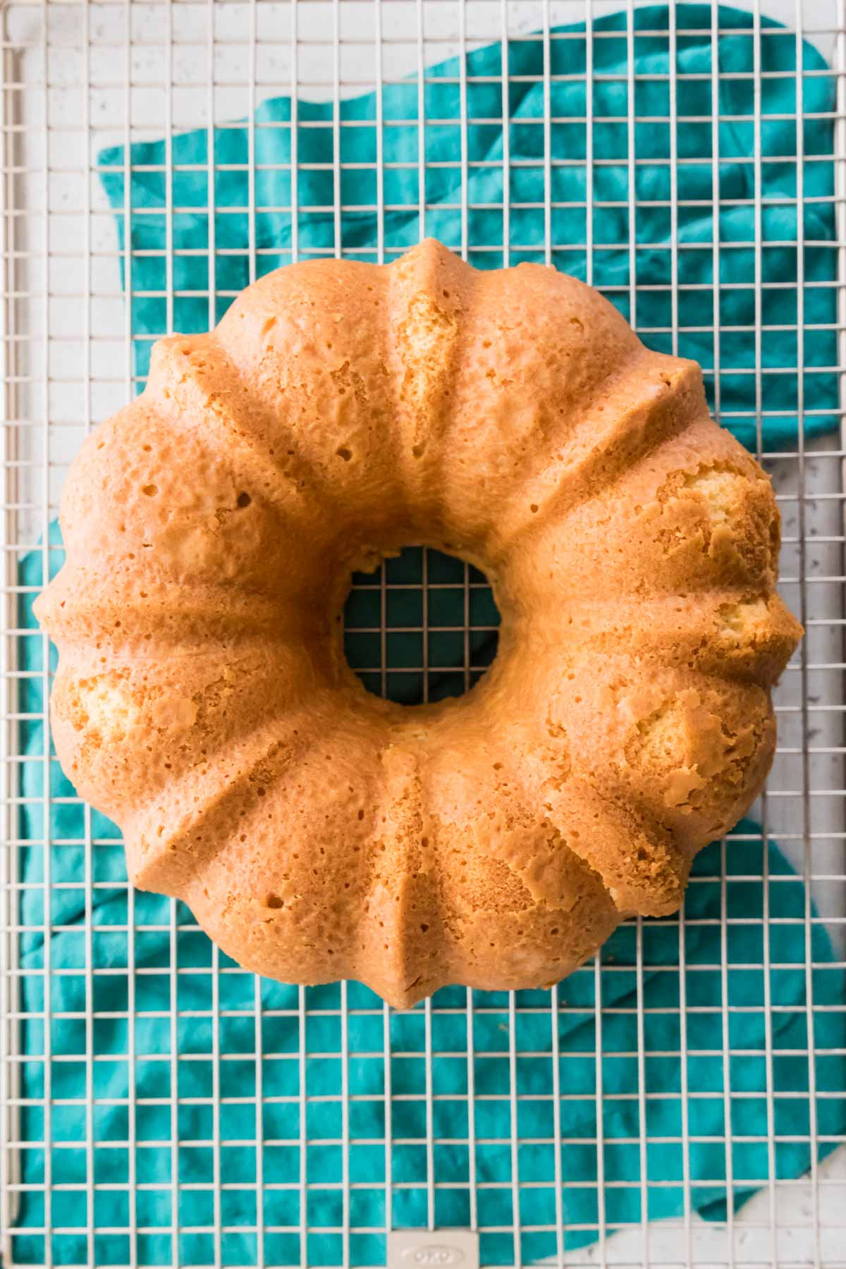 overhead view of a whole golden brown bundt cake on a cooling rack with a teal towel underneath