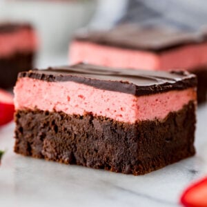 close-up view of a strawberry brownie consisting of a brownie layer, strawberry icing layer, and a final layer of chocolate ganache