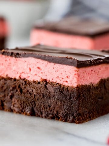 close-up view of a strawberry brownie consisting of a brownie layer, strawberry icing layer, and a final layer of chocolate ganache