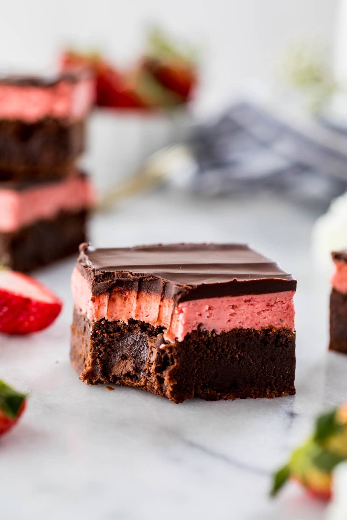 thick, square-cut brownie layered with pink strawberry frosting and chocolate ganache with a bite missing from one corner