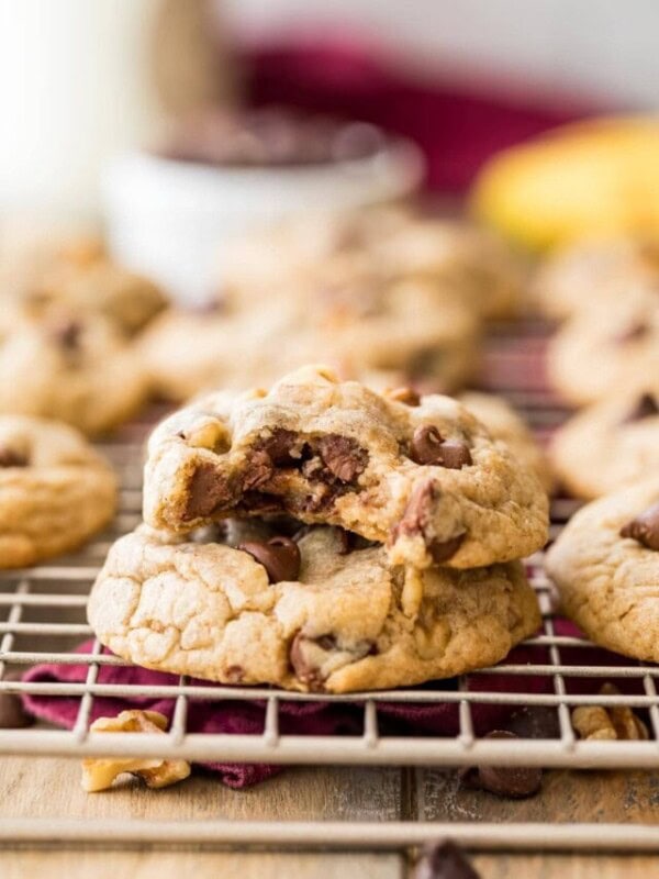 two cookies filled with chocolate chips and walnuts stacked on top of each other, with the top cookie missing a bite
