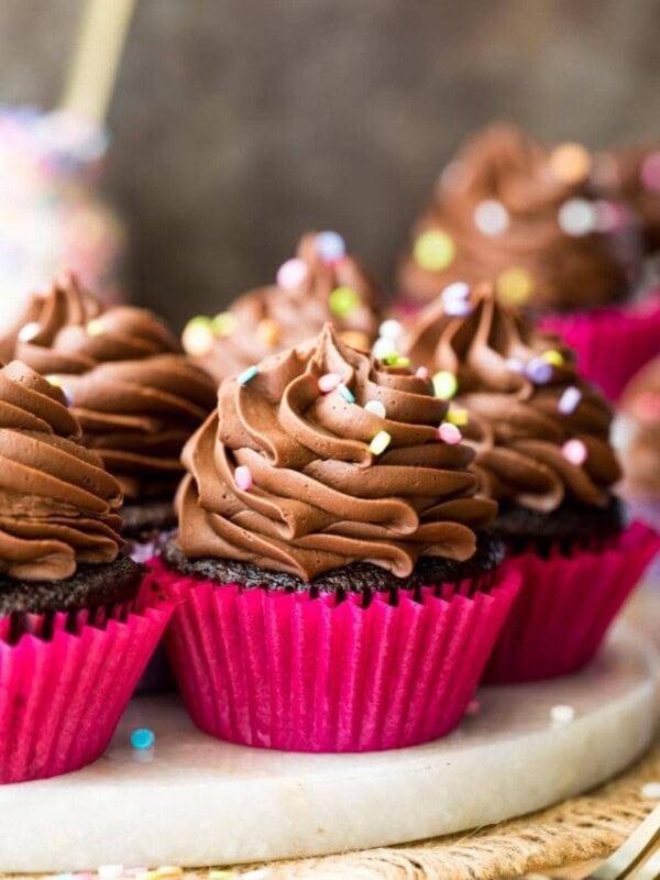 three chocolatey cupcakes topped with chocolate frosting and sprinkles on a white platter
