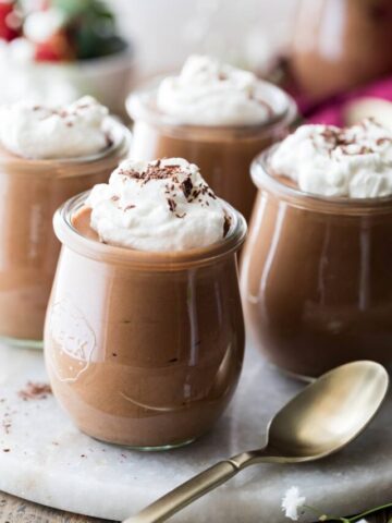 whipped cream topped chocolate desserts served in small glass jars