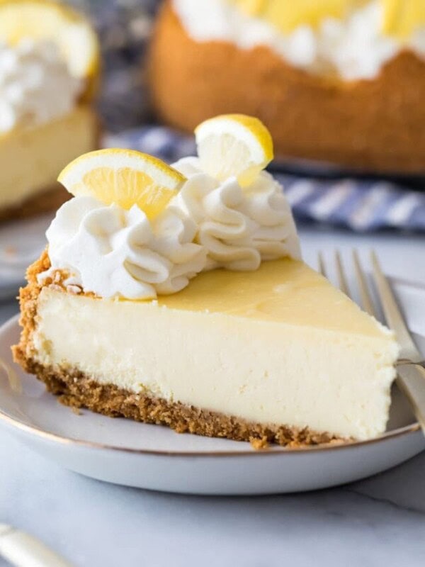 slice of lemon cheesecake topped with whipped cream and sliced lemon wedges
