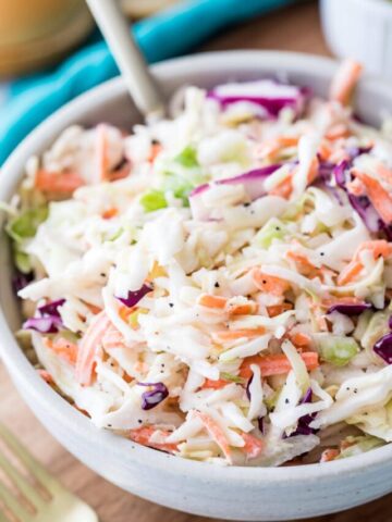 large bowl of homemade coleslaw full of shredded green and purple cabbage, carrots, and creamy dressing co