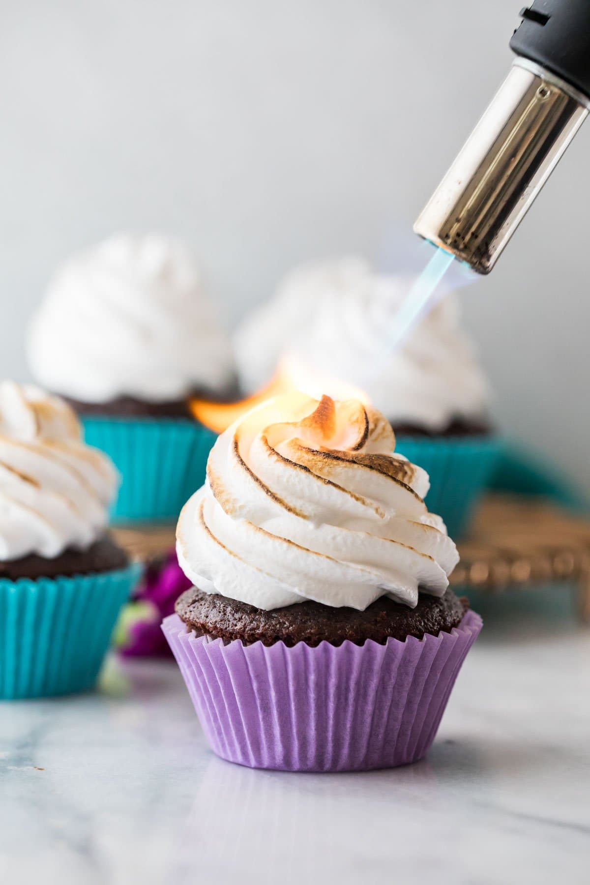 culinary torch toasting a marshmallow frosting swirl on top of a chocolate cupcake