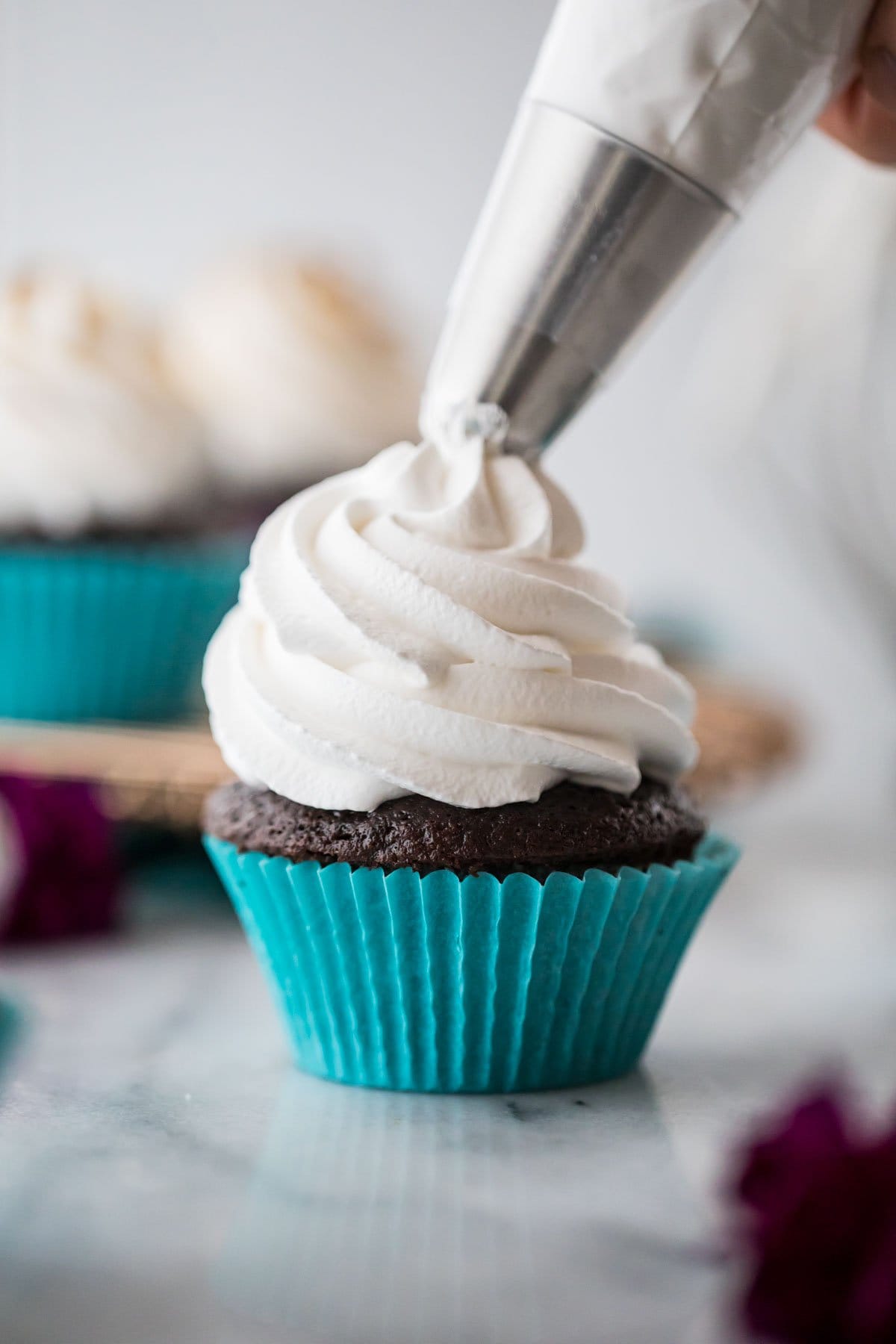 white frosting being piped onto a chocolate cupcake