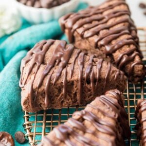 three wedge-shaped chocolate scones drizzled with a chocolate glaze on a metal cooling rack