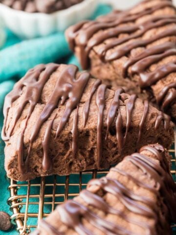 three wedge-shaped chocolate scones drizzled with a chocolate glaze on a metal cooling rack