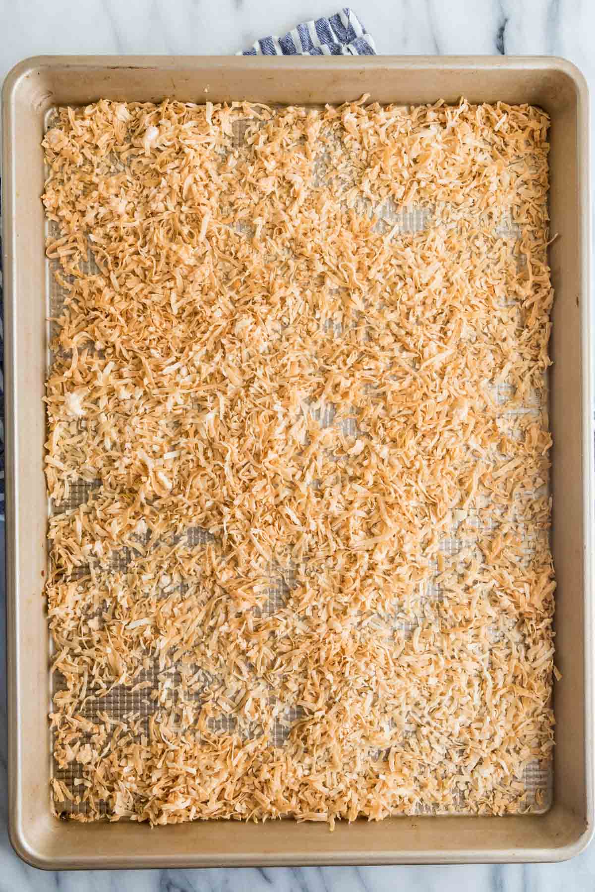 cookie sheet covered with shredded coconut after its been toasted in the oven