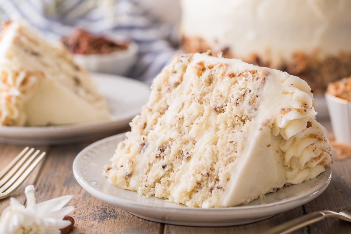 slice of cake consisting of three layers studded with coconut and chopped pecans frosted with cream cheese frosting