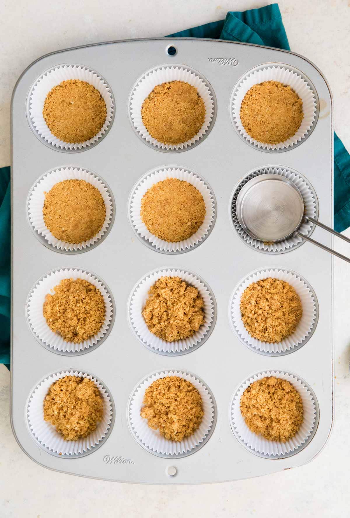 overhead view of graham cracker crumbs being pressed into a muffin pan