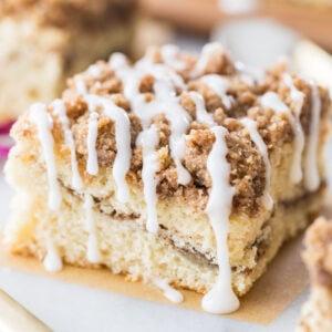 square slice of coffee cake with a cinnamon swirl middle, crumb topping, and vanilla drizzle glaze