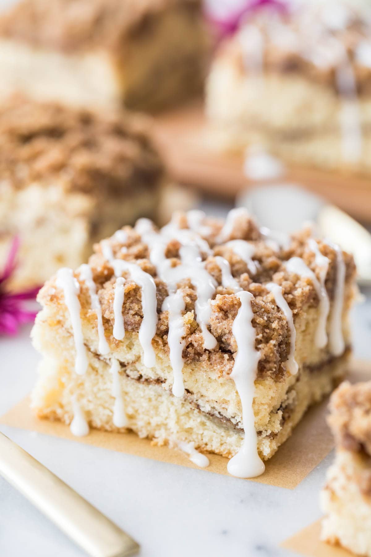 square slice of coffee cake with a cinnamon swirl middle, crumb topping, and vanilla drizzle glaze