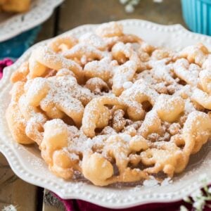 golden brown funnel cake dusted with powdered sugar on a white plate