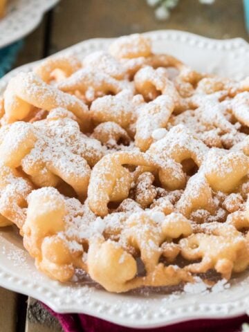 golden brown funnel cake dusted with powdered sugar on a white plate