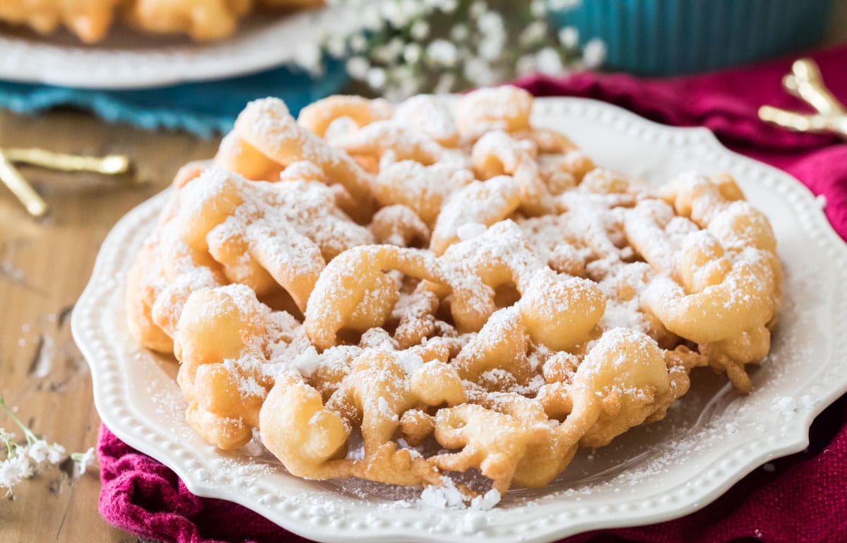 powdered sugar covered homemade funnel cake on a white plate