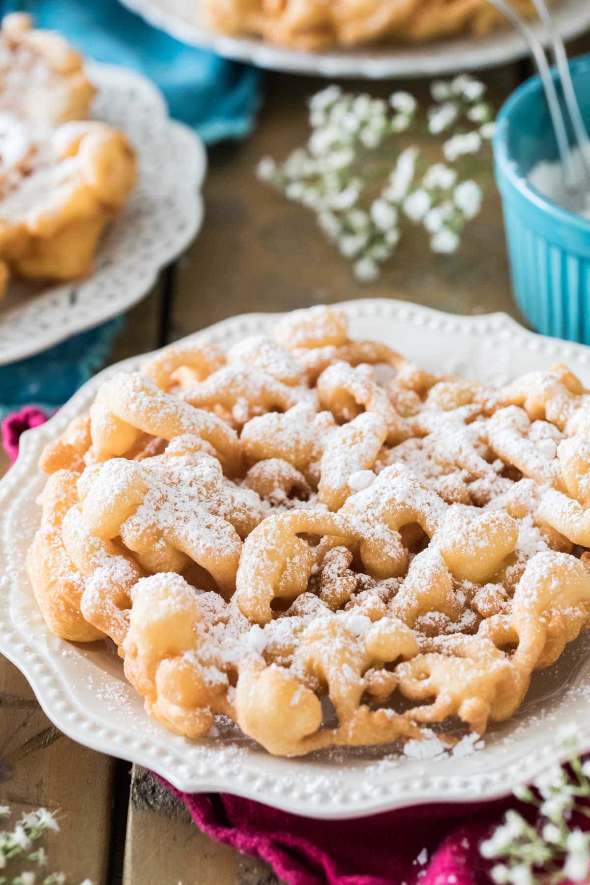 golden brown funnel cake dusted with powdered sugar on a white plate