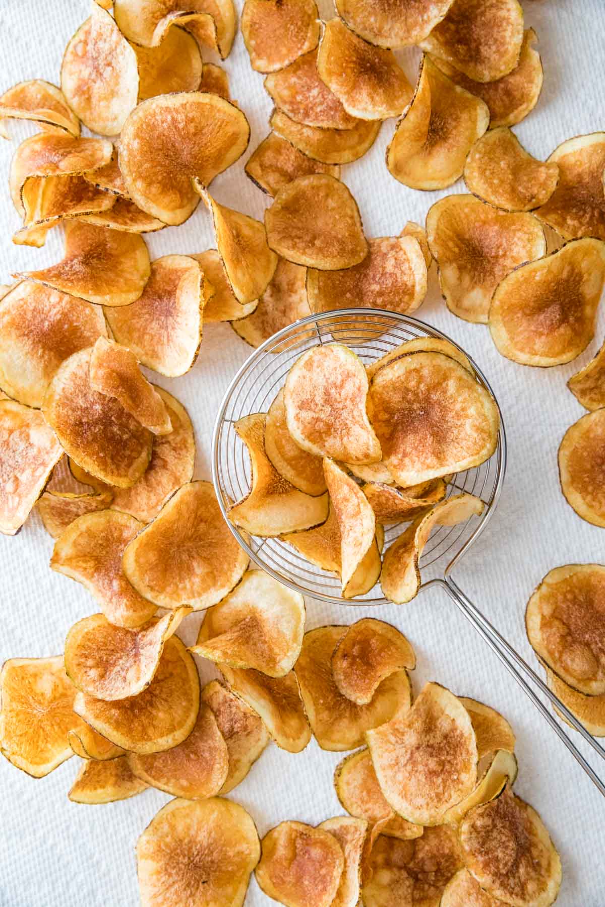 overhead view of homemade potato chips surrounding a frying spider on paper towels