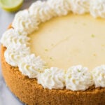 close-up view of a whole key lime cheesecake topped with a decorative whipped cream border and lime zest