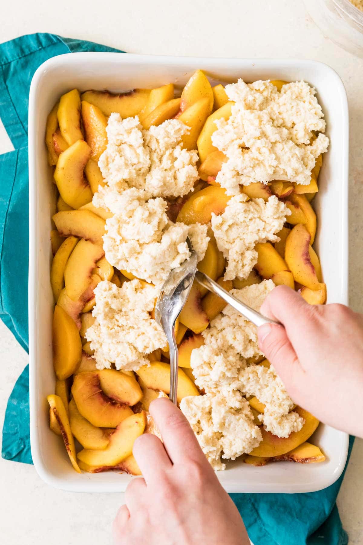 overhead view of cobbler topping being spooned onto peaches