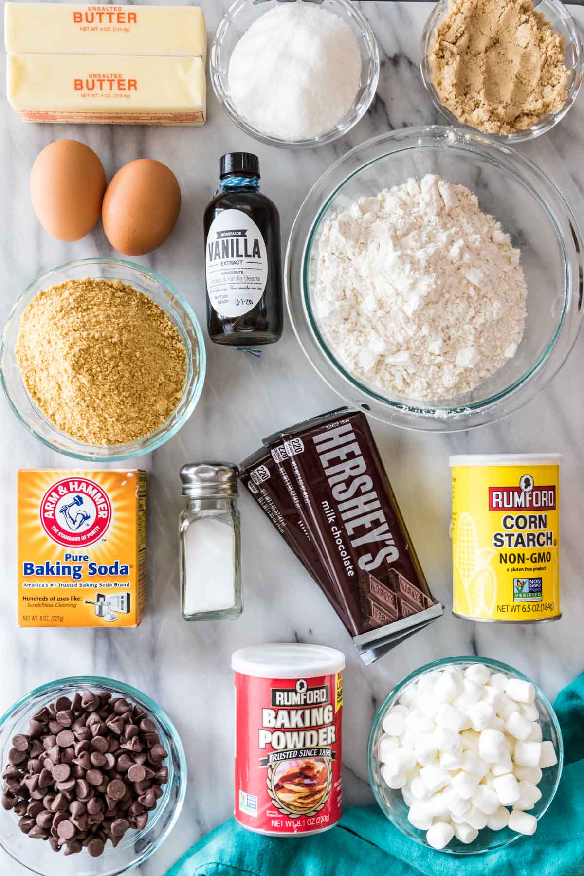 overhead view of ingredients including graham cracker crumbs, hershey bars, marshmallows, flour, and more