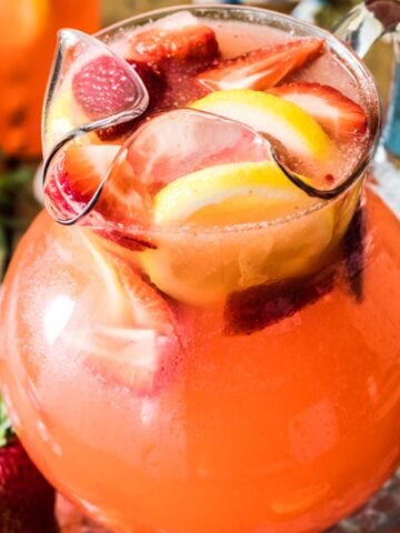 large glass pitcher of homemade strawberry lemonade with sliced strawberries and lemons as a garnish