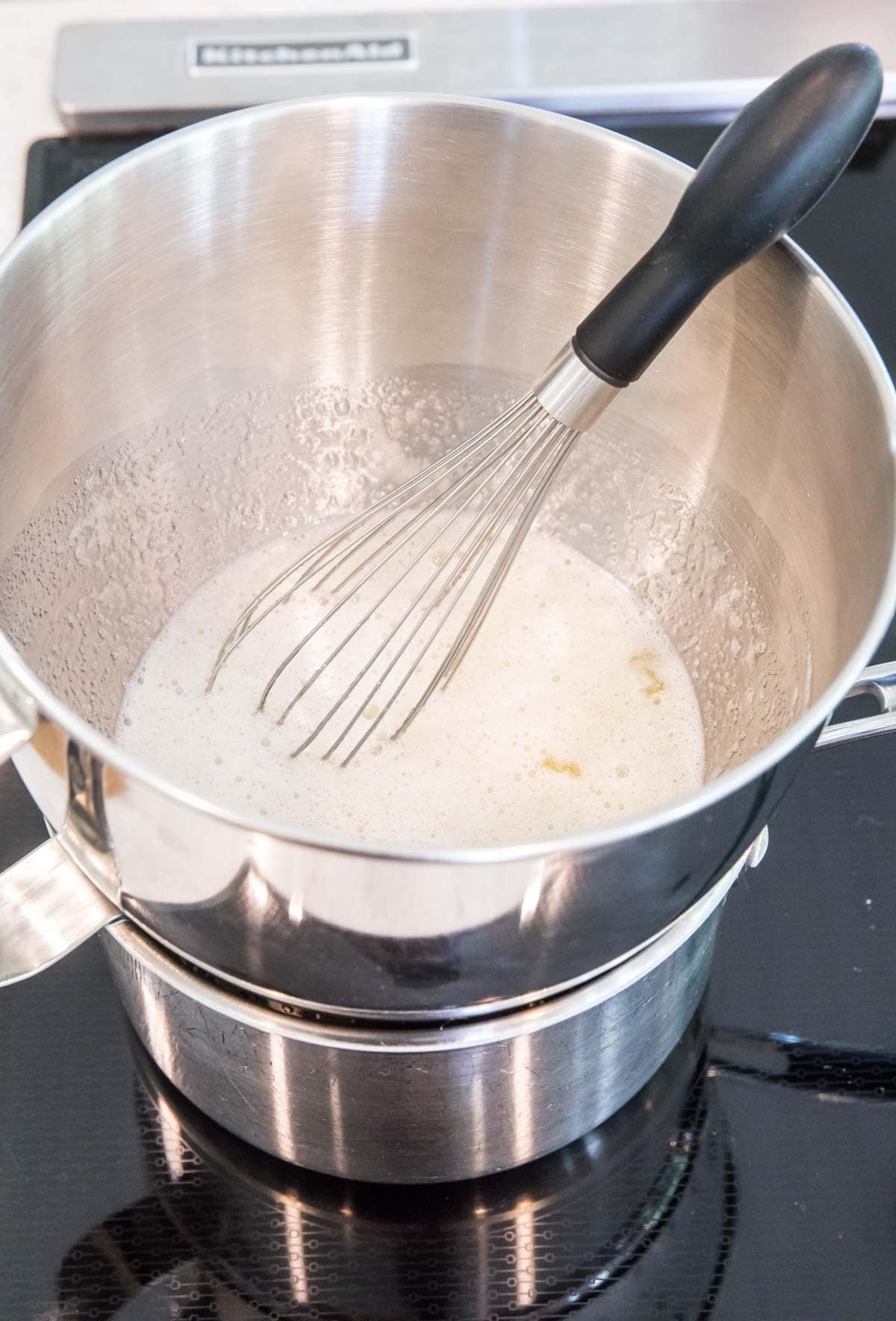 double boiler setup with a whisk resting in a sugar and egg white mixture