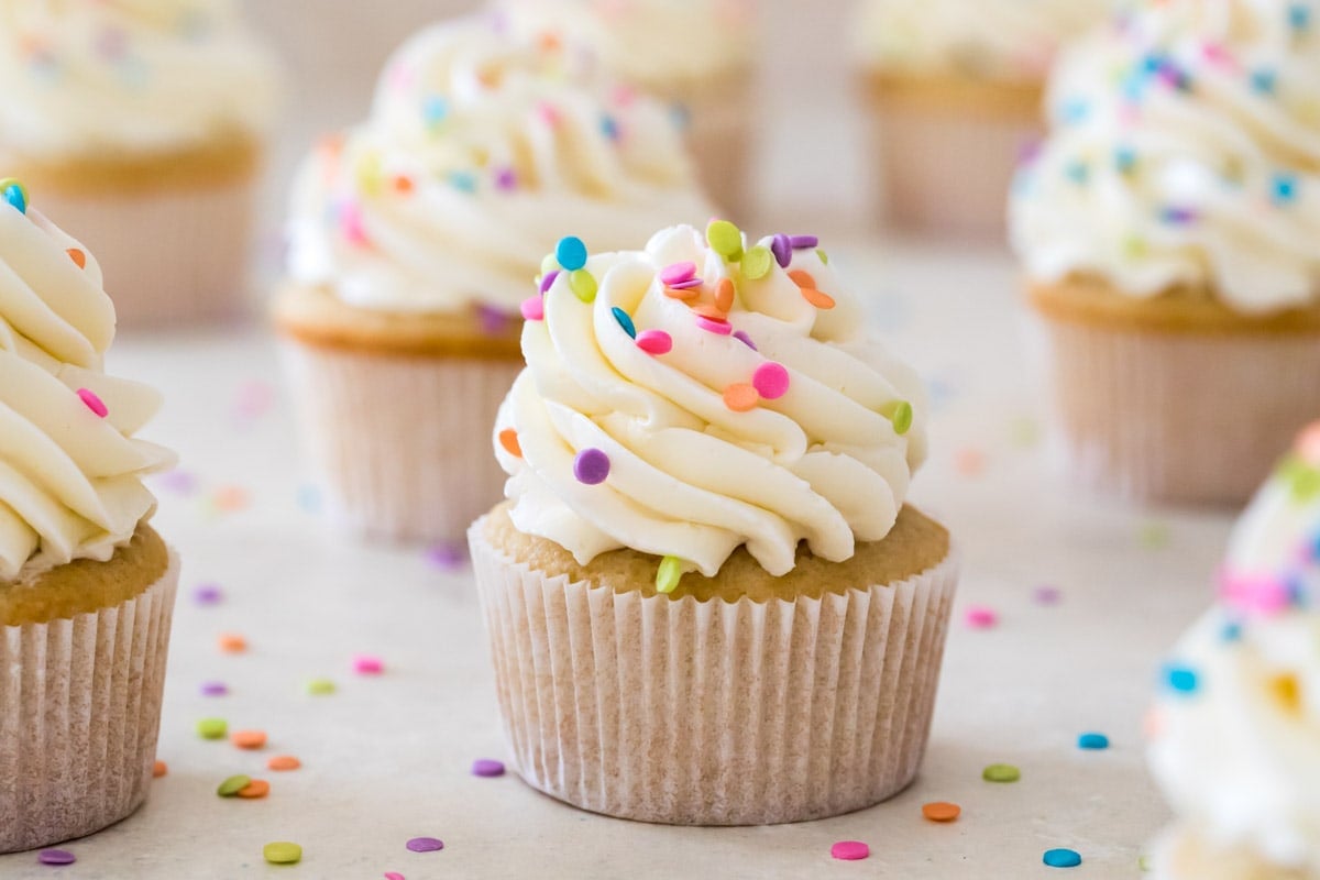 vanilla cupcakes topped with lots of piped icing and rainbow sprinkles