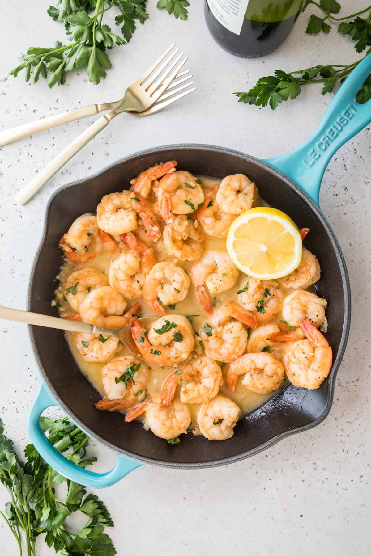 overhead view of a skillet full of cooked shrimp topped with parsley and lemon