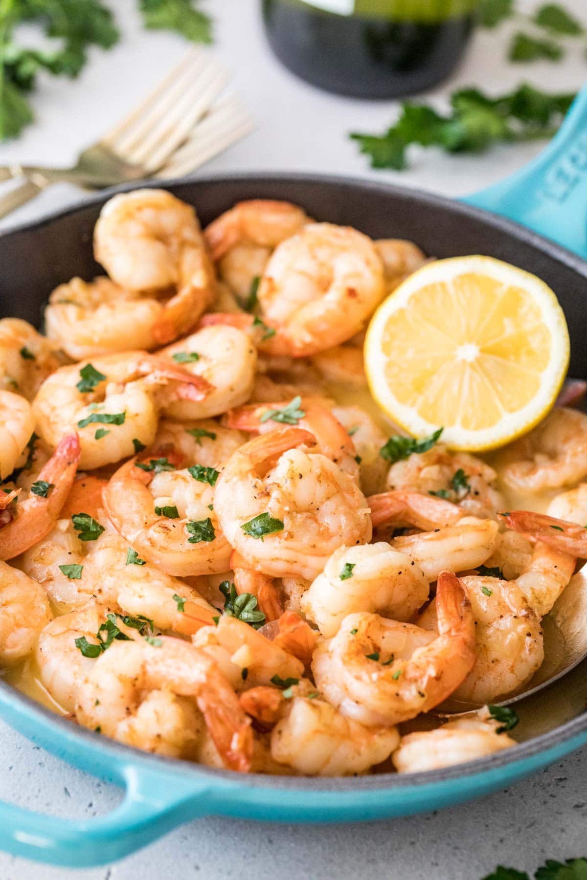 skillet full of cooked shrimp topped with parsley and lemon