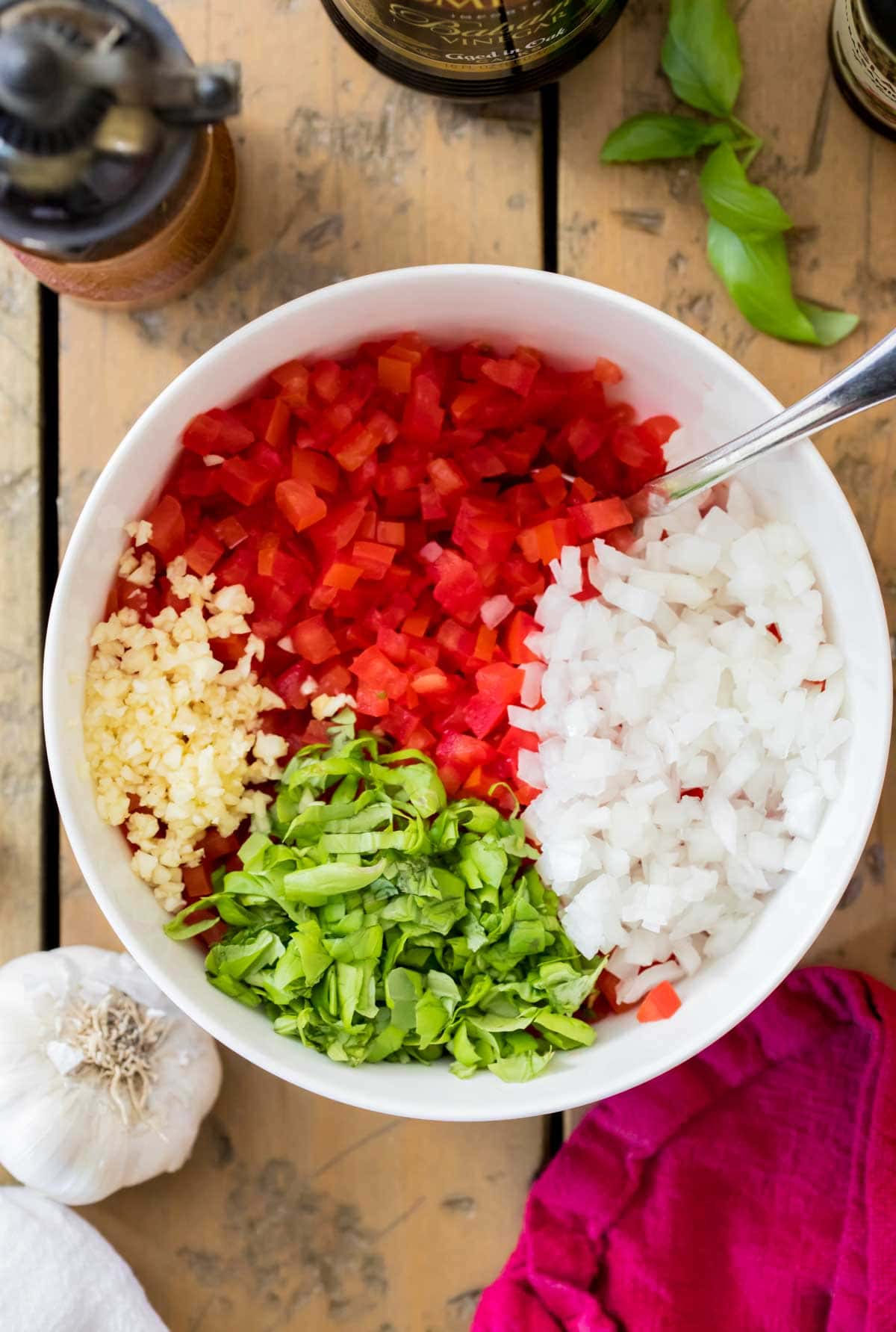 overhead view of ingredients in a bowl before mixing, including chopped tomatoes, onion, basil, and garlic