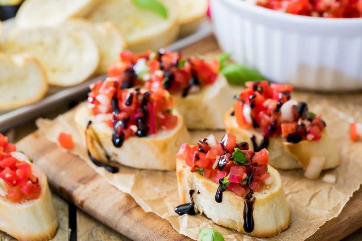 slices of bruschetta topped with chopped marinated tomatoes, basil, and garlic with a balsamic drizzle