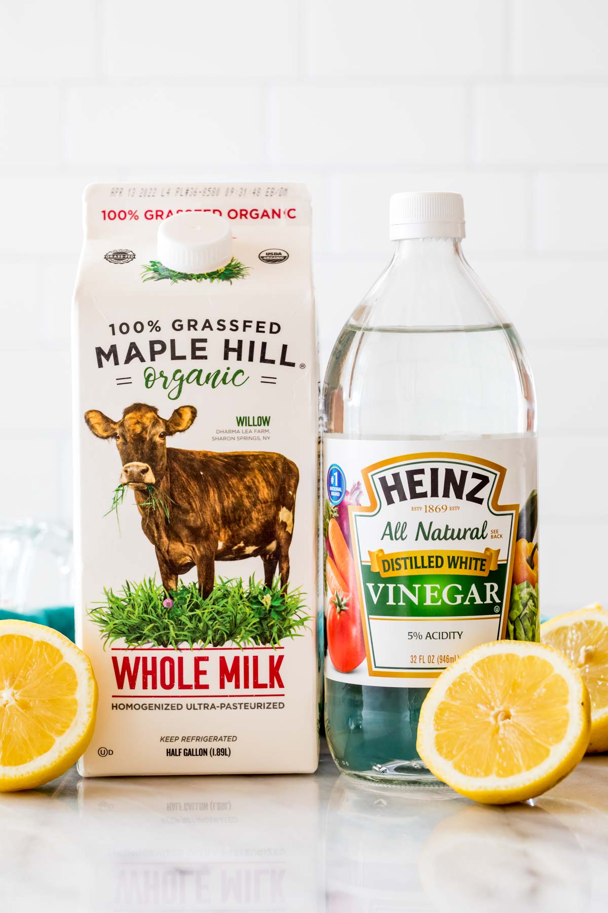 whole milk bottle and white vinegar bottle standing beside each other with cut lemon halves scattered around them