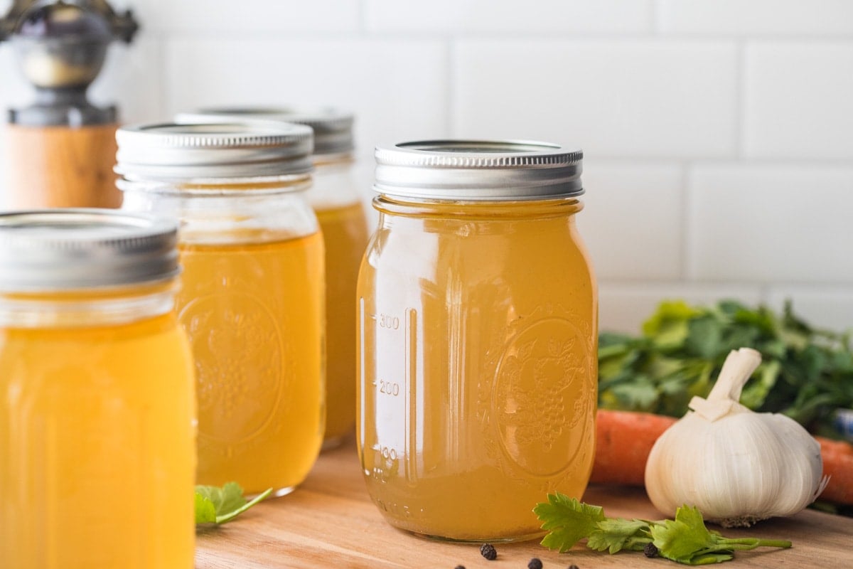 large mason jars of chicken stock beside veggies