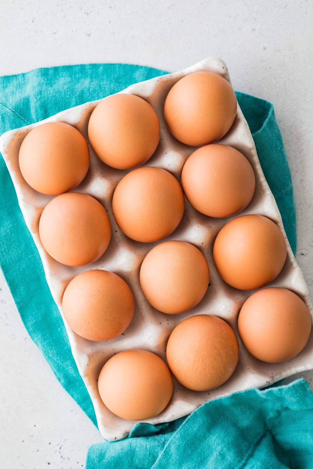 overhead view of brown eggs in an egg carton on a teal towel