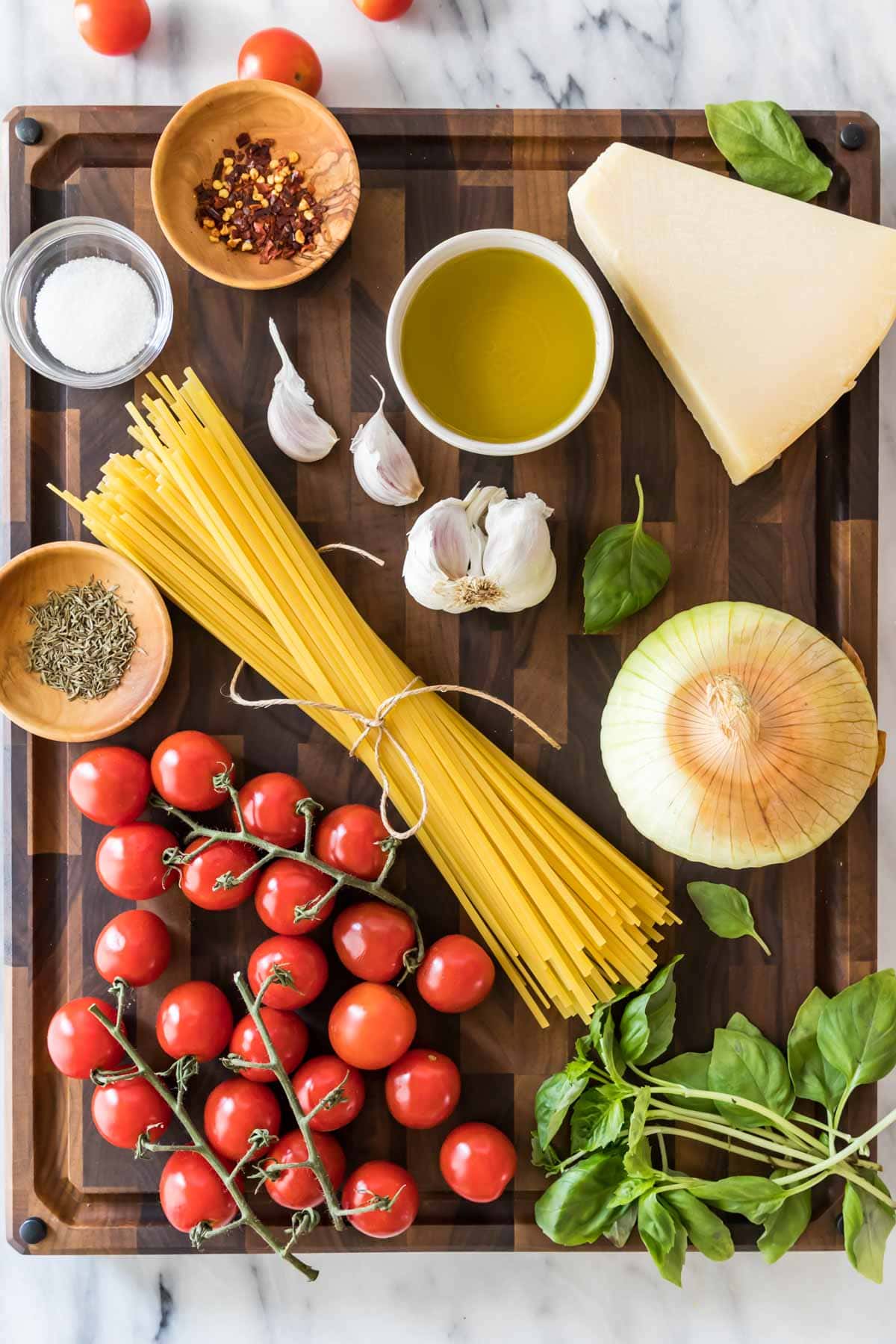 overhead view of ingredients including linguine pasta, cherry tomatoes, basil, and more