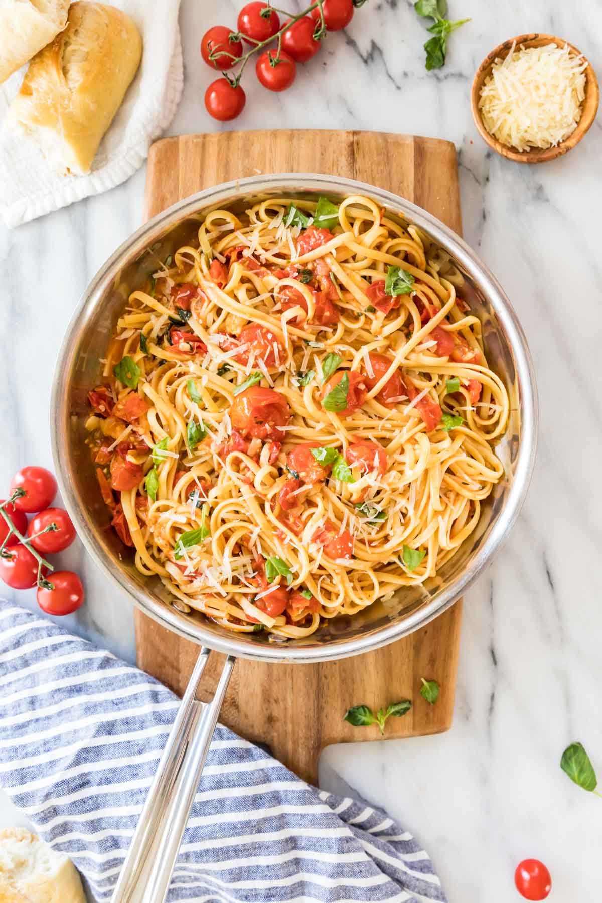 overhead view of a stainless steel skillet of linguine pasta with cherry tomatoes and fresh basil