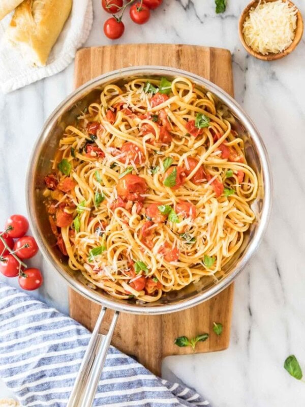overhead view of a stainless steel skillet of linguine pasta with cherry tomatoes and fresh basil