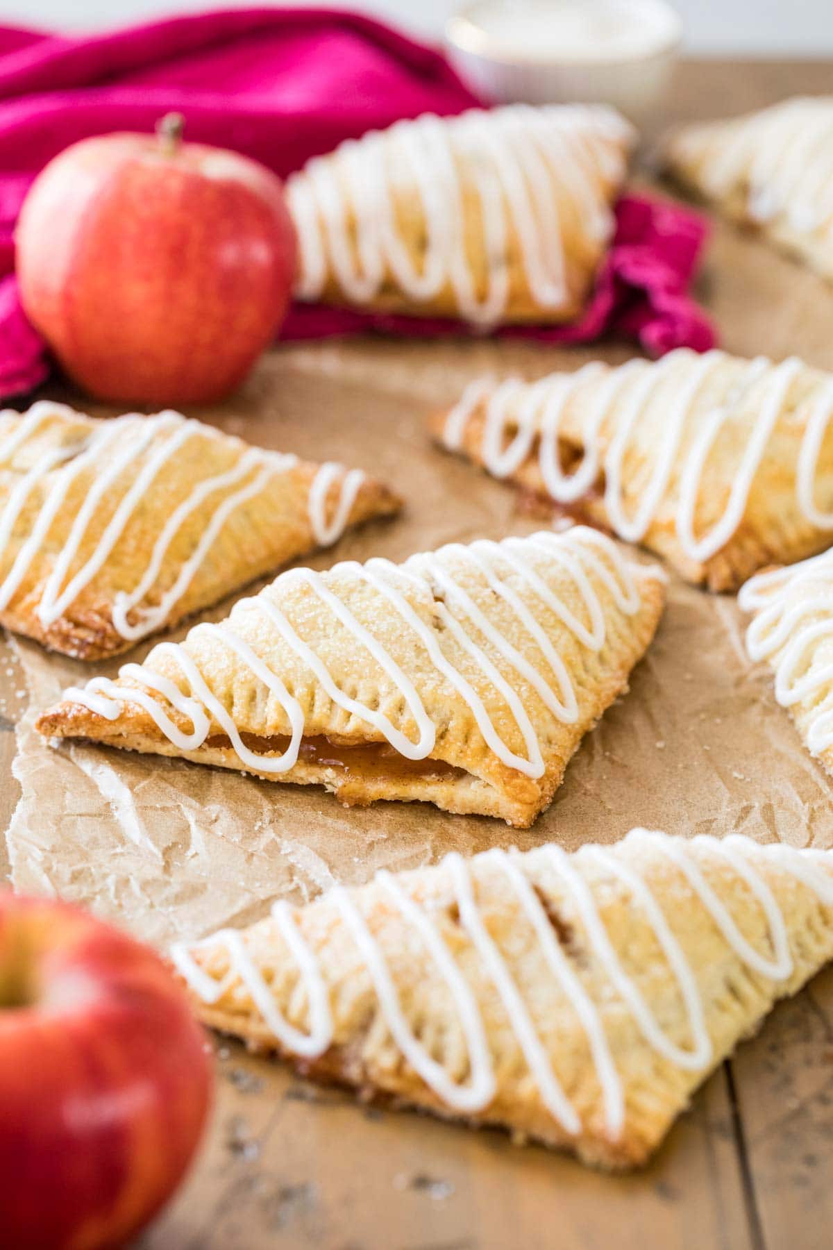 homemade turnovers that have been sprinkled with sugar and glazed resting on brown parchment paper